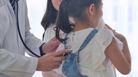 亚洲男性儿科医生和小女孩6岁的母亲访问医疗诊所而医生检查儿童与听诊器检查心跳和肺部在医院的医学检查医患会诊概念