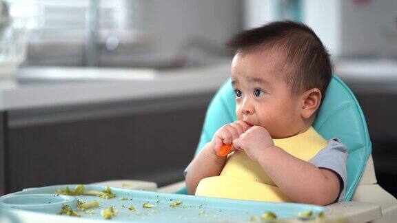 宝宝看了看手里的胡萝卜第一次吃泥他的亚洲小男孩的母亲喂养婴儿食品