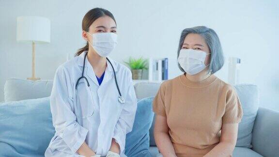 老年女病人与医生坐在一起的画像看护者治疗师药剂师女孩戴口罩看望和服务治疗老年女性微笑看着相机