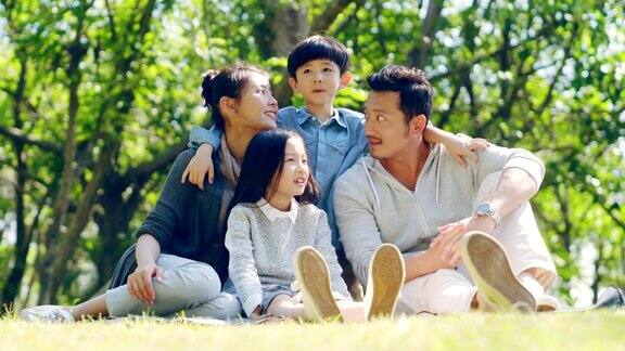 亚洲家庭坐在公园户外的草地上