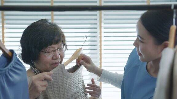 有吸引力的年轻老年亚洲公民和搓洗护士的家庭护理或协助生活帮助老年女性选择穿衣在早上例行与亚洲老年护理概念
