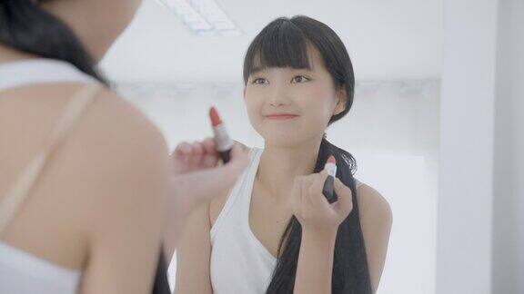 美丽年轻的亚洲女性涂口红在嘴上美丽的女孩看着镜子的脸化妆化妆品与嘴唇的优雅化妆与性感的女性皮肤护理和健康的理念