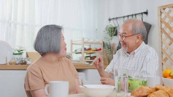 亚洲老年夫妇在家里的厨房里一起吃沙拉幸福的家庭有魅力的年长成熟的夫妻坐在餐桌上享受退休生活午餐吃健康的食物在家里