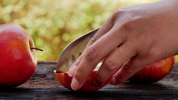 女人在木桌上用尖刀切红苹果