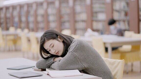 疲惫的大学生躺在图书馆的书桌前