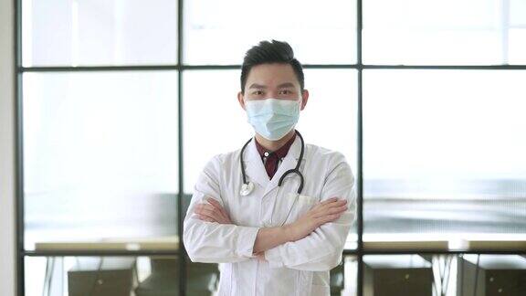 亚洲华人男医生戴着口罩在医生办公室看着摄像机