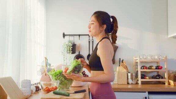亚洲有吸引力的运动妇女拿着沙拉碗和吃蔬菜美丽的运动女孩穿着运动服享受吃干净的蔬菜后在家里的健康饮食和健康食品