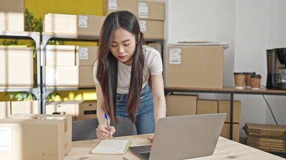 年轻的中国女性电子商务工作人员在办公室用笔记本电脑写笔记