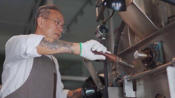 低角度看亚洲华人高级工匠微笑着拿着特里尔从咖啡烘焙机中提取咖啡豆烘焙生咖啡豆闻检查