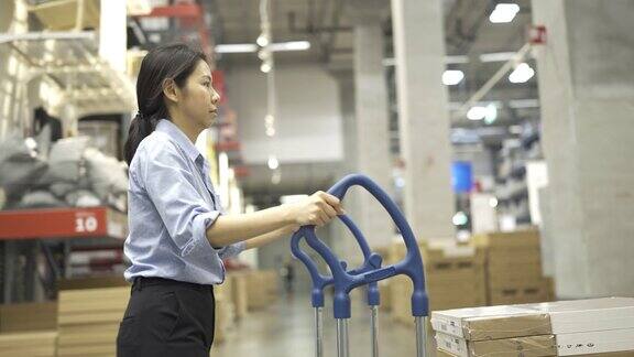 4K女性仓库工人使用手推车在仓库中移动商品