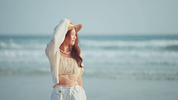 快乐的亚洲年轻女子戴着草帽漫步在热带海滩上无忧无虑的女性微笑着享受着以海为背景的微风旅游度假夏日户外娱乐