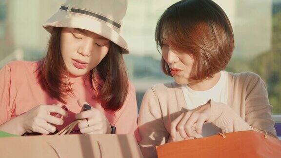 两个年轻的亚洲女人在地铁上展示她们在购物袋里买的新东西慢镜头