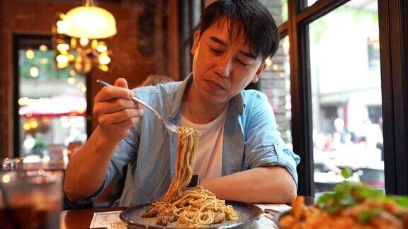 年轻的亚洲男子一边吃面条一边看手机