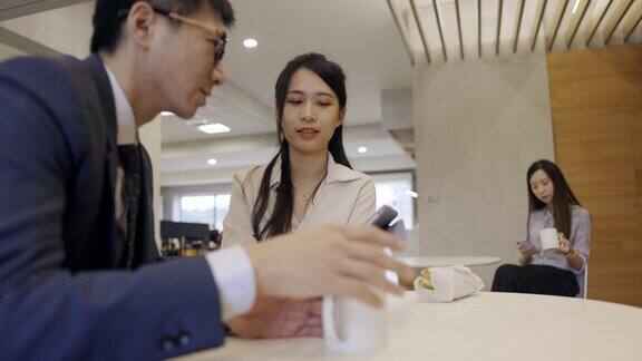 两名亚洲白领坐在公司的休息室里讨论一份商业计划清单