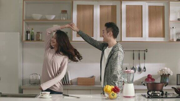 快乐的年轻亚洲夫妇在家里的厨房里跳舞