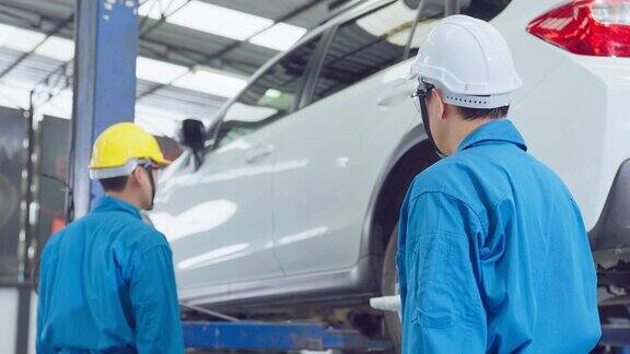 亚洲两名汽车机械师男子戴着头盔在机械厂工作车辆维修经理男工组在车况下检查维修车间的发动机