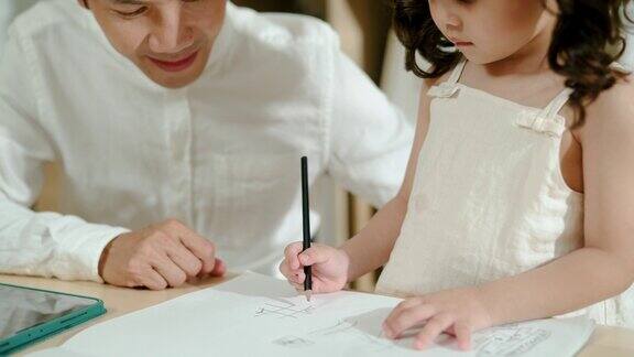 年轻的亚洲父亲在客厅教女儿用铅笔画画