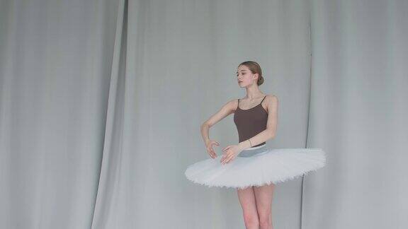 芭蕾舞女演员在浅色背景下用手表演流畅的动作在宽敞的大厅里优雅地排练着白天鹅的角色近距离