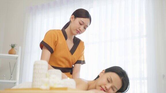 亚洲年轻女性感到快乐和放松在背部按摩油迷人的美女躺在按摩台上在温泉美容院接受按摩师的皮肤和身体护理