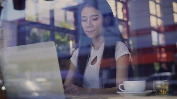 美丽的亚洲女性自由职业者使用她的笔记本电脑和在咖啡店工作透过玻璃与反射
