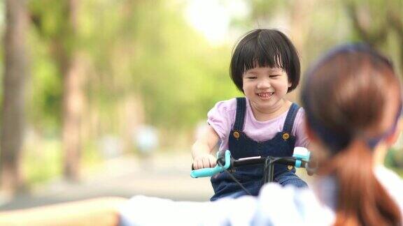 亚洲小女孩和妈妈在花园里骑自行车双臂伸展