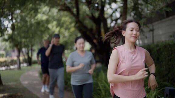 在一个温暖的日子里女儿妈妈、爸爸和儿子在公园里慢跑的慢动作广角跟踪镜头