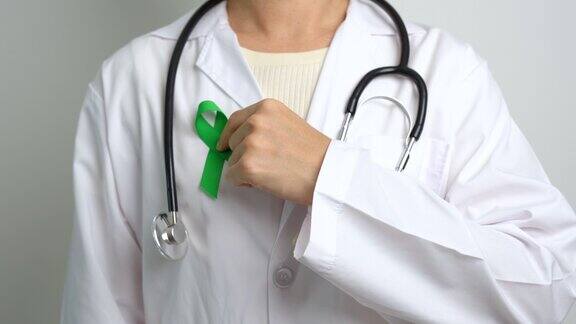 为世界精神卫生日、肝脏、胆囊、胆管、子宫颈癌、肾癌和淋巴瘤宣传月佩戴绿丝带的医生保健和世界癌症日概念