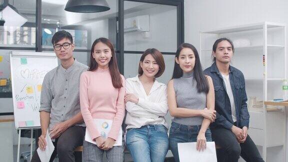 亚洲青年创意人士在智能休闲装看相机和微笑在创意办公室的工作场所不同的亚洲男性和女性站在一起创业