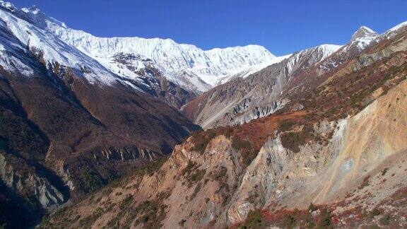 阳光明媚的日子里喜马拉雅山脉的风景深谷环绕着岩石斜坡和积雪山脊马南山谷安纳普尔纳环行尼泊尔