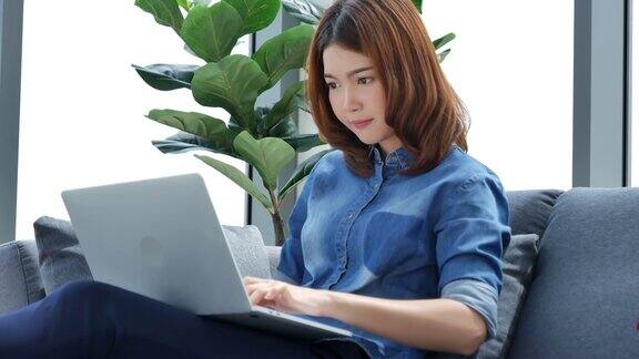 妇女在家工作的笔记本电脑在线会议在家庭办公室亚洲女企业家用笔记本电脑坐在沙发上科技新常态的生活方式快乐的女人打字键盘笔记本电脑
