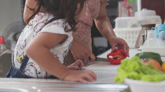 亚洲母亲教她的女儿清洁和切片蔬菜在厨房家庭