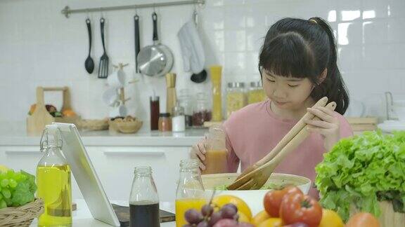 一个亚洲小女孩在家厨房做饭的时候在平板电脑上看沙拉食谱
