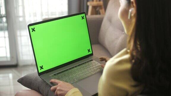 亚洲妇女坐在沙发上使用绿色屏幕的笔记本电脑