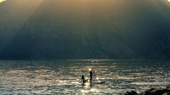 日落时分加尔达湖上沿着山脉的站立桨板上的游客