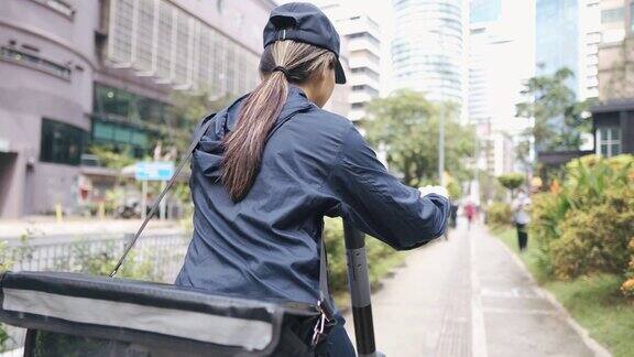 亚洲华人女性送货员在城市中以电动滑板车为交通工具的移动中查看订单地址