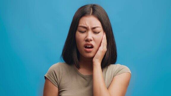 不幸的年轻亚洲妇女触摸脸颊遭受牙痛有可怕的突然牙齿疼痛