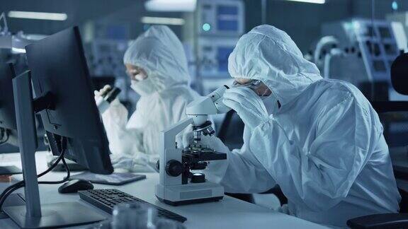 研究工厂洁净室:工程师科学家穿着工作服和手套使用显微镜检查主板微处理器组件开发高科技现代电子
