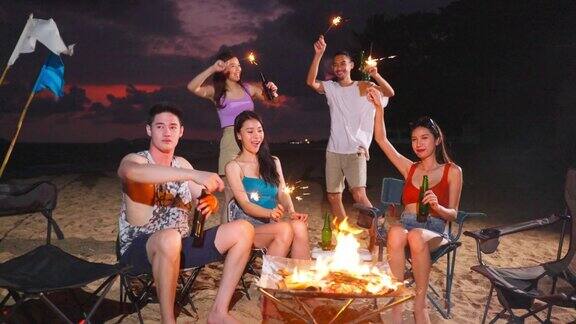 一群亚洲年轻男女晚上在海滩上聚会迷人的朋友们在海边露营时唱歌跳舞一起在热带海岛度假度假