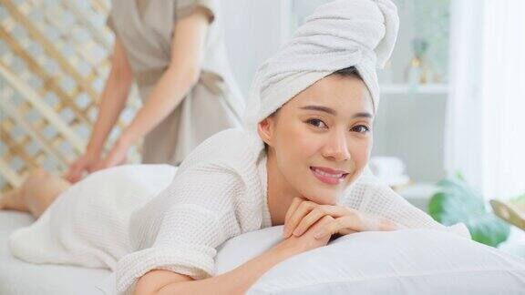 亚洲年轻女性感到快乐和放松在背部按摩油美丽迷人的女孩躺在按摩台上在spa美容院接受按摩师的皮肤和身体护理
