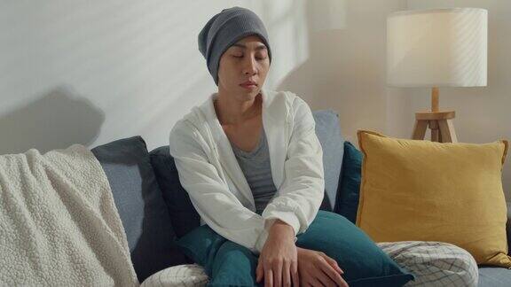 绝望的年轻亚洲妇女患有癌症坐在家里客厅的沙发上