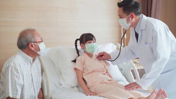 亚洲男医生带着口罩来到康复室向躺在病床上的儿童病人询问健康问题