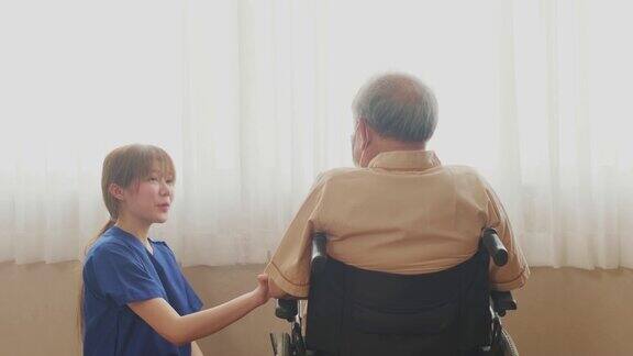 在医院照顾坐在轮椅上的成熟男性病人的亚洲护士年轻女子推着轮椅然后坐下来微笑着和老人交谈待客医疗服务理念