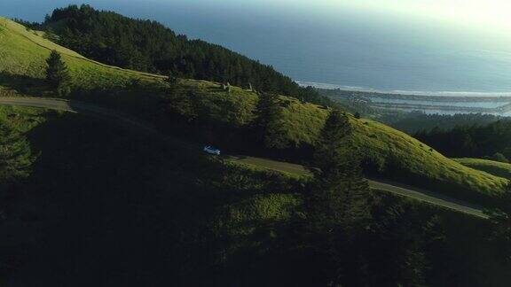 鸟瞰图的汽车驾驶下的乡村道路通过农村起伏的山与海洋的背景在日落