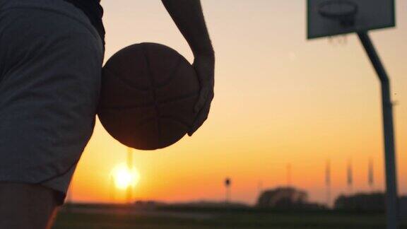 日落时分一名年轻人带着篮球走出户外篮球场