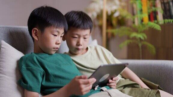 两个亚洲男孩坐在沙发上玩数码平板电脑