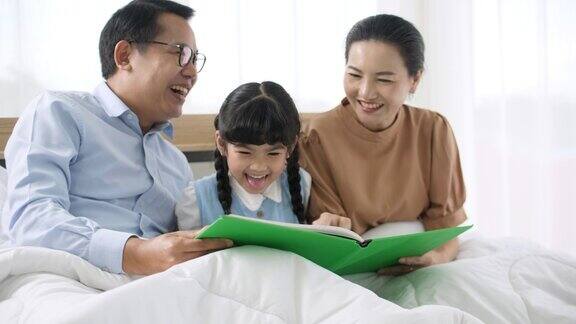 幸福的家庭父母和他们的小女儿在床上看书