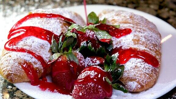 把草莓糖浆倒在白色盘子里的甜羊角面包上美味的羊角面包作为早餐或零食
