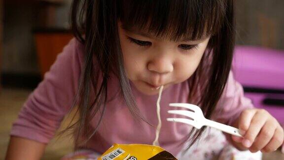 亚洲小女孩有乐趣吃面条在塑料杯在家里垃圾食品