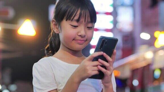10岁的亚洲女孩晚上在城市里使用5G智能手机的幸福可视化5g