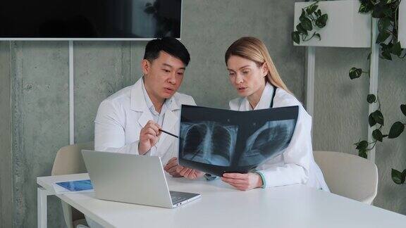 两个不同的医生交谈和使用笔记本电脑分析病人的x光片谈结果分析医疗保健诊所亚洲主任外科医生和放射科医生讨论咨询病人的肺部图像